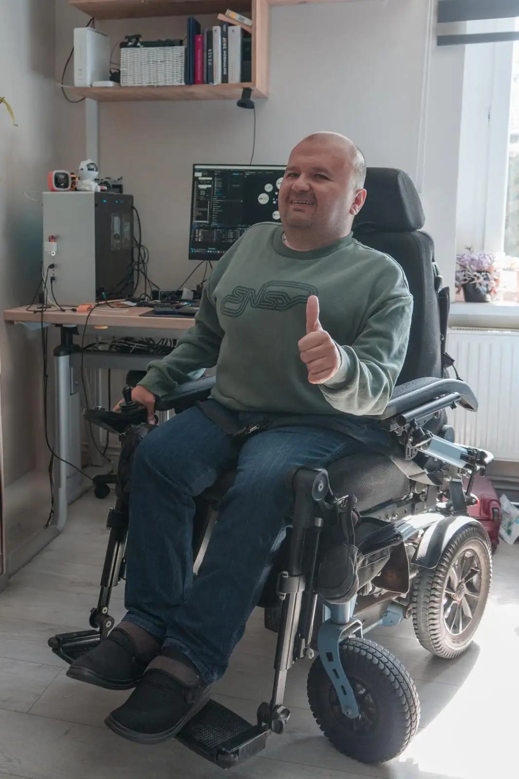 Konrad uśmiecha się w swojej pracowni, siedząc na wózku elektrycznym